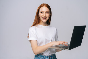 Charming young woman student holding laptop computer and looking away on isolated gray background....