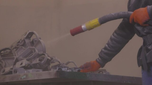 The man is sandblasting the detail. Sandblast metal parts. Sandblasting gun