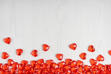 Small red heart shape transparent candies or glass decorations laying on white wooden background at bottom side as a lovely greeting card on saint valentine's day. Image with copy space, horizontal