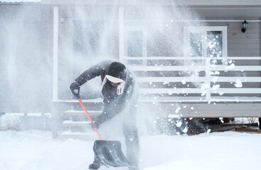clearing snow near the house after a heavy snowfall. a man shovels snow near a wooden house.