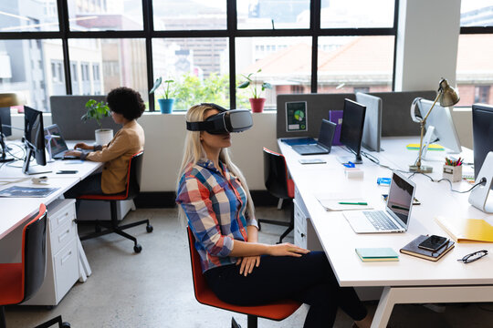 Caucasian businesswoman sitting at desk in office wearing vr headset