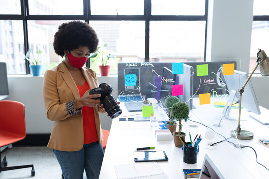 Mixed race businesswoman wearing face mask using camera in creative office
