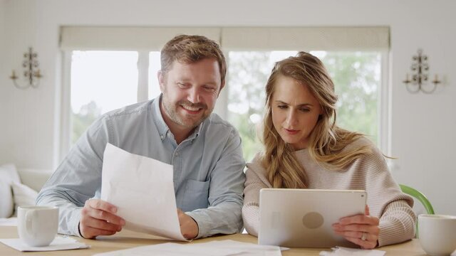 Couple with digital tablet sitting at table at home reviewing domestic finances together - shot in slow motion