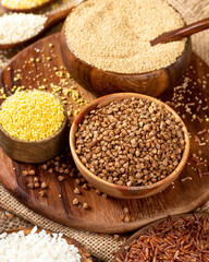White and red rice, buckwheat, amaranth seeds, corn groats, quinoa and millet in bowls on a brown wooden table. Gluten-free cereals. Closeup	