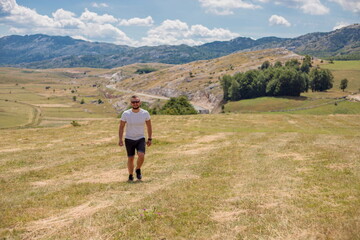  Man walking on the field on the mountain in autumn or summer day. Beautiful landscape in Montenegro.