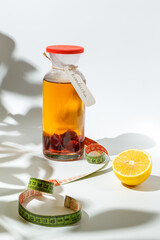 Homemade kombucha lemonade with berries and lemon, in a glass bottle. On a white background with pretty shadows from the plants with a measuring tape