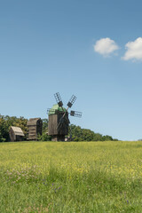 Fototapeta premium Old wodden windmill on a green meadow, field. Blue sky with white clouds.