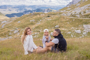 Naklejka na ściany i meble Family sitting on the meadow grass and looking at the beautiful mountain view. Have fun together,spent time, laughing,smiling and enjoy the life. Durmitor, Montenegro.