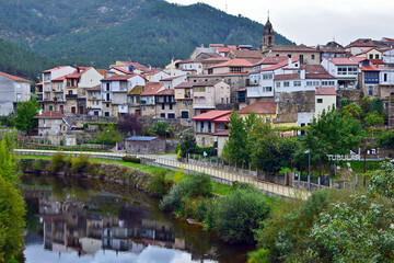 Fototapeta na wymiar Church and houses in a rural mountain village with a river and a path for walking. Some houses are reflected in the river