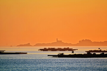 Sea landscape at dusk. Silhouettes of fishing platforms and an island with a lighthouse in the distance