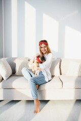 Cheerful young woman holding her big puppy with black nose and laughing. Indoor portrait of smiling girl posing with french bulldog
