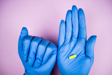 hands with blue latex gloves holding a yellow medicine pill in the palm with pink background