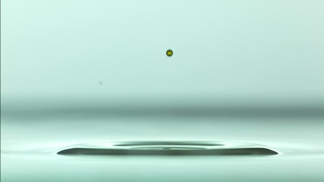 Close up of a yellow water droplet falling In teal water In super slow motion