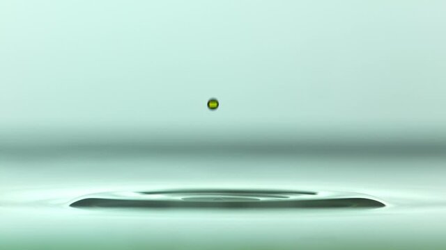 Close up of a yellow water droplet falling In teal water In super slow motion