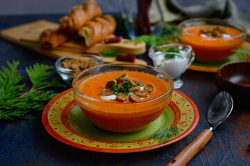Closeup of orange puree soup with baked peppers and tomatoes on beautiful plates with croutons and sour cream sauce. Still life.