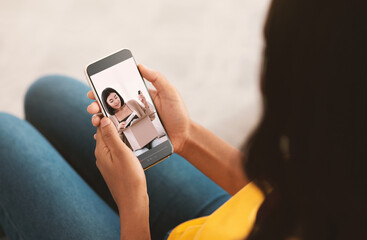Young black woman watching video review of skincare products by popular beauty blogger on smartphone