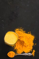 Turmeric latte, a golden milky hot healthy drink on a dark background in a glass tumbler