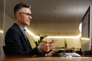 Smiling grey man using mobile phone while working with computer