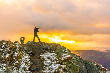 A photographer on top of the mountain in the snowy winter orange sunset, on Mount Peñas de Aya in the town of Oiartzun near San Sebastián, Gipuzkoa. Basque Country