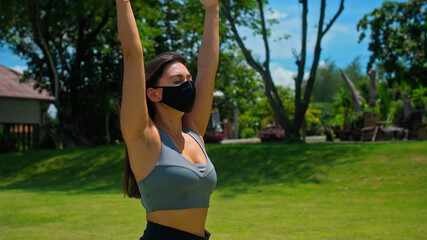 Young European brunette girl practices alone yoga in nature wearing a black protective mask
