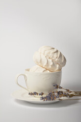 Old cup filled with souffle airy dessert zefir (zephyr) made of organic pectin and egg whites, similarly to marshmallow and meringue. Served with lavender on tea plate, isolated on white background
