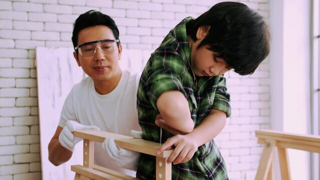 Young male carpenter teaching his son how to work with wood in workshop.