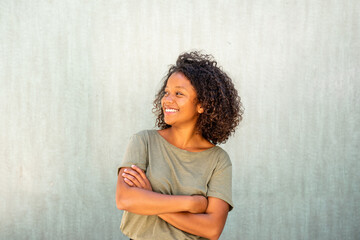 cool young African American woman with arms crossed and looking away by green background