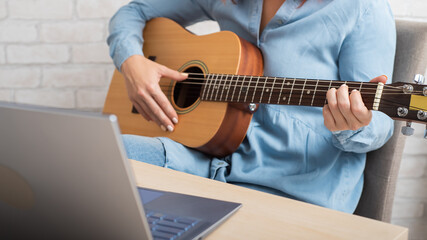 A woman teaches to play the guitar online. Remote music lessons on a laptop