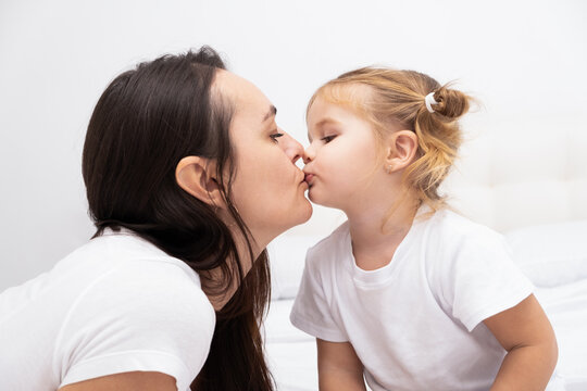 adult brunet mother kissing her little blond daughter, white background.