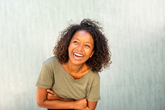cheerful young African American woman laughing with arms crossed by green background