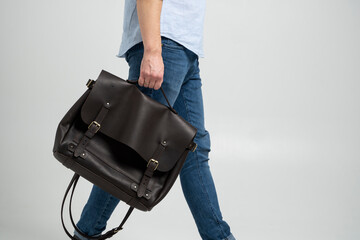 Brown men's shoulder leather bag for a documents and laptop holds by man in a blue shirt and jeans with a white background. Satchel, mens leather handmade briefcase.