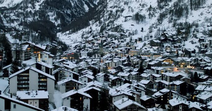 Cityscape of the Swiss village of Zermatt in Valais in winter, at dawn with snow and illuminations. The Matterhorn and the Alpine mountain range in the background.