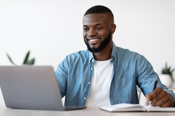 Black Millennial Male Entrepreneur Taking Notes While Working On Laptop In Office