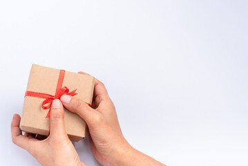 A close-up of a woman's hand holding a small gift wrapped in a red ribbon.