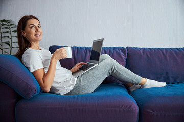 Relaxed woman with hot drink and laptop indoors