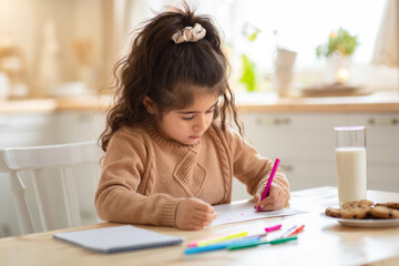 Indoor Portrait Of Small Adorable Girl Drawing Picture At Table In Kitchen