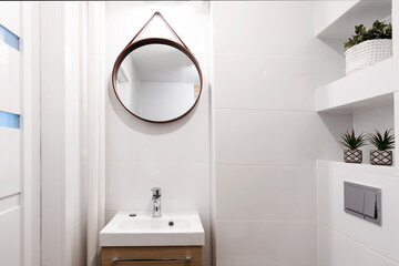 Small bathroom with bathroom sink and round mirror on the wall. White tiles and ceramic wash basin in modern interior.