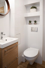 Modern bathroom interior in hotel. Small bathroom with white tiles, ceramic sink, wooden cabinet, round mirror and toilet. Vertical