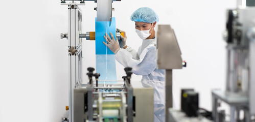 Professional Asian engineering man in sterile cloths and face mask working and control machine in surgical mask factory. industry factory and people concept. indoors