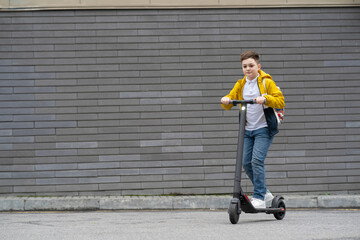 Obraz na płótnie Canvas Modern teenager with backpack rides on electric scooter on brick wall background