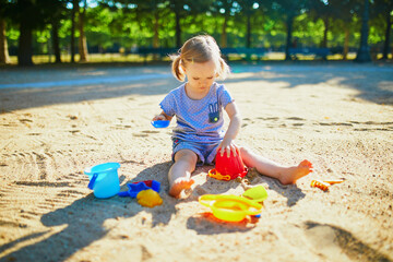 Adorable little girl having fun on playground in sandpit