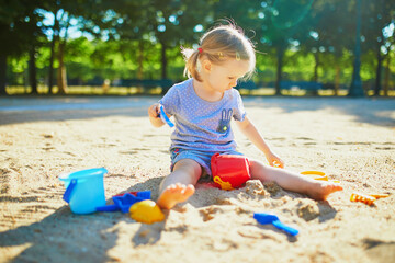 Adorable little girl having fun on playground in sandpit