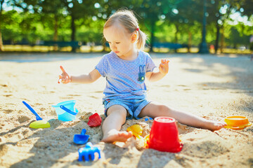 Adorable little girl having fun on playground in sandpit