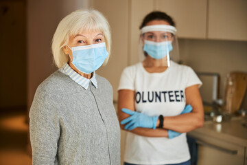 Fototapeta na wymiar Volunteer in latex gloves standing behind a senior lady