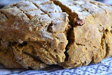 Loaf of round grammed rye and wheat bread on a white tablecloth with a blue ethnic pattern
