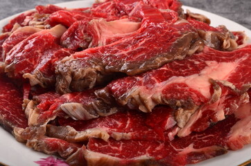 Obraz premium Thinly cut raw meat slices on a white plate, gray background