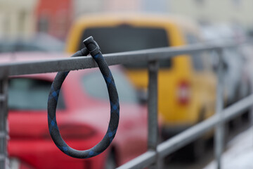 Thick round bike lock covered in white frost hanging on metal handrail in city with cars in...