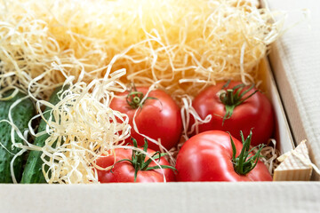 Wooden and cardboard crate box with fresh ripe tasty red tomatoes and green cucumbers with wood...