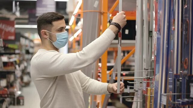 Young carpenter wearing disposable medical mask holding a builders level in a hardware store.
