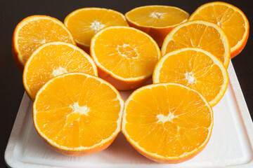 Nice composition of fresh oranges cut in half on a white cutting board on the dark kitchen table. Preparation of healthy juices.